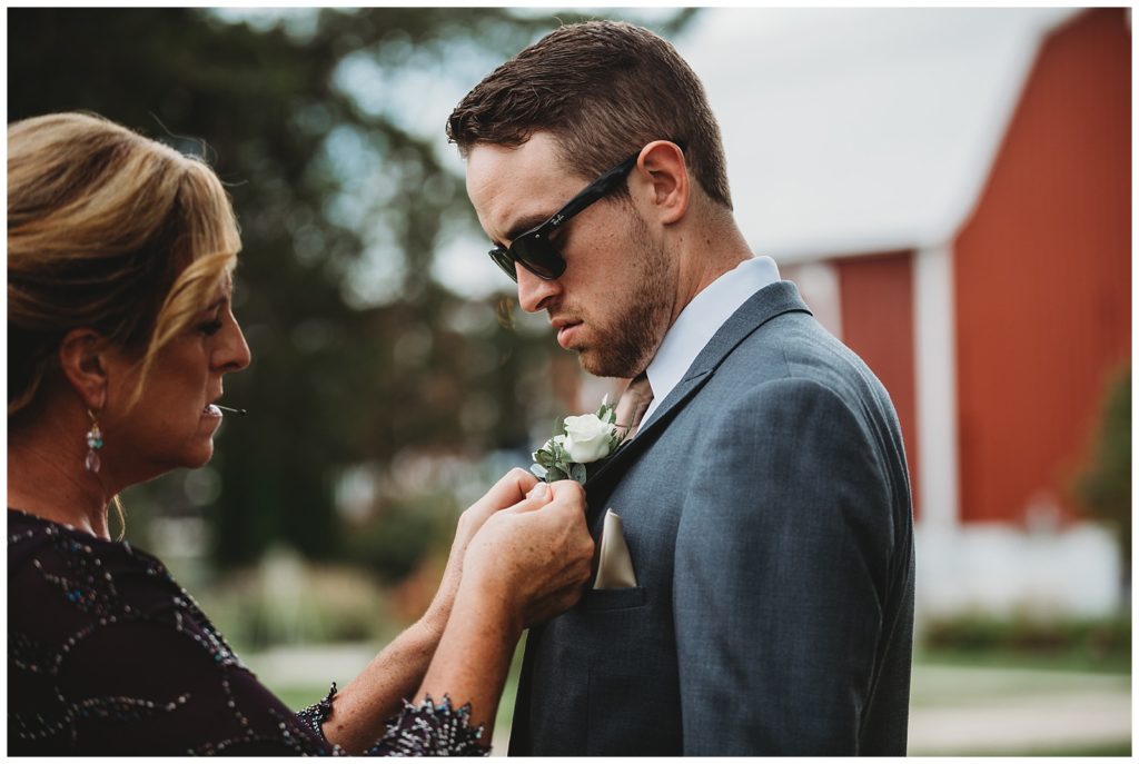 boutonnière being pinned onto grooms jacket by mom