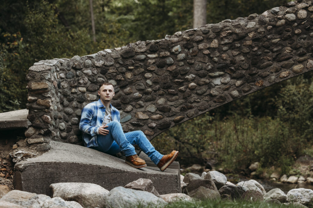 boy sitting on rock near bridge for senior photo